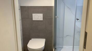 A bathroom with a toilet, a shower with a glass door, and a tiled floor.