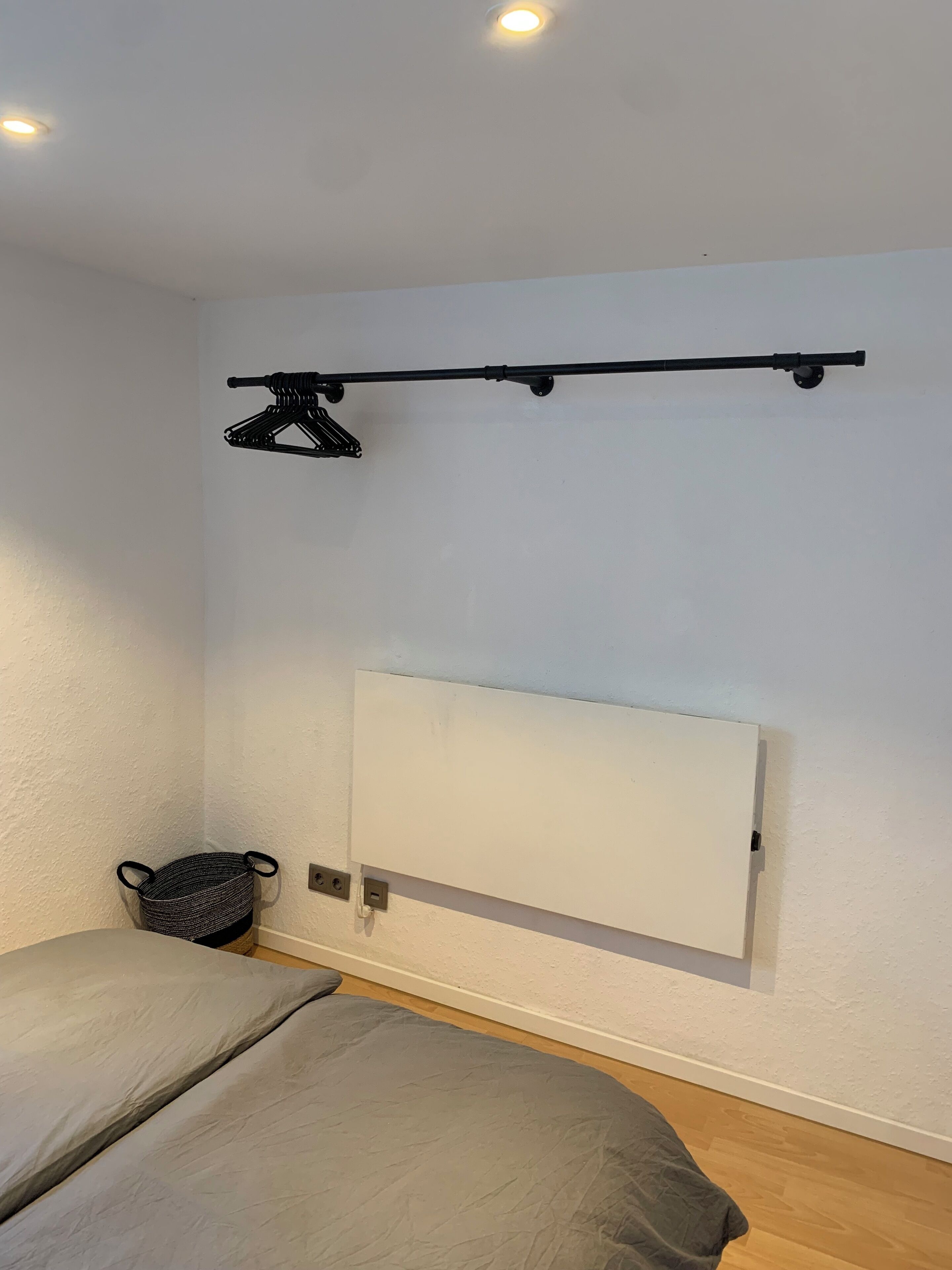 A small, simple room with a bed, a wall-mounted shelf, and a power outlet.