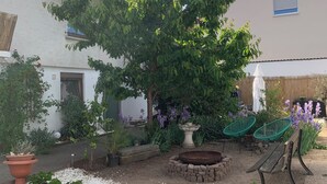 Ein Innenhof mit einem großen Baum, einer Steinsitzbank, einem Holztisch und einem kleinen Brunnen.