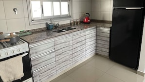 A modern kitchen with a gas stove, stainless steel sink, and black refrigerator. - MORON GRAN ATARDECER APARTMENT (Morón)