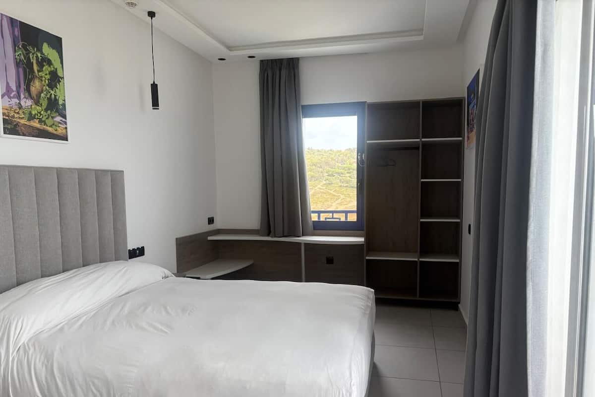 A hotel room with a bed, a desk, a wardrobe, and a window with curtains.