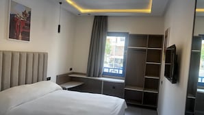 Une chambre d’hôtel moderne équipée d’un lit, d’une télévision, d’une fenêtre avec des rideaux et d’une armoire intégrée.