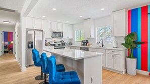 A modern kitchen with white cabinets, a central island with blue bar stools, and a colorful accent wall.