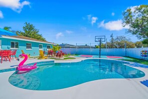 Piscina com boia de flamingos cor-de-rosa, cadeiras vermelhas e um aro de basquete.