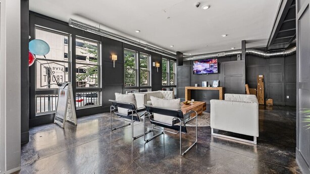 A modern living room with a black leather sofa, a white armchair, and a coffee table. There is a television mounted on the wall and a fireplace. - Modern Loft Retreat Steps from Memphis Hotspots (Memphis)