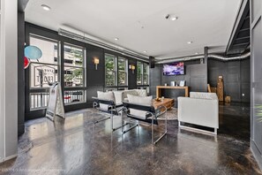 A modern living room with a black leather sofa, a white armchair, and a coffee table. There is a television mounted on the wall and a fireplace. - Modern Loft Retreat Steps from Memphis Hotspots (Memphis)