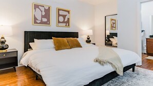 A modern bedroom with a large bed, two bedside tables, a nightstand, a mirror, and abstract wall art. - Modern Loft Retreat Steps from Memphis Hotspots (Memphis)