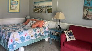 A bedroom with a bed, a red couch, a nightstand, and wall art. - Ground floor, poolside unit #143. Beach and sound access. Great getaway! (Atlantic Beach)