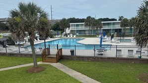 A swimming pool with lounge chairs, a wooden deck, and a building in the background. - Ground floor, poolside unit #143. Beach and sound access. Great getaway! (Atlantic Beach)