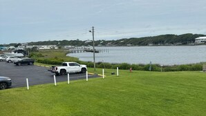 A grassy area with a dock extending into a body of water, surrounded by buildings. - Ground floor, poolside unit #143. Beach and sound access. Great getaway! (Atlantic Beach)