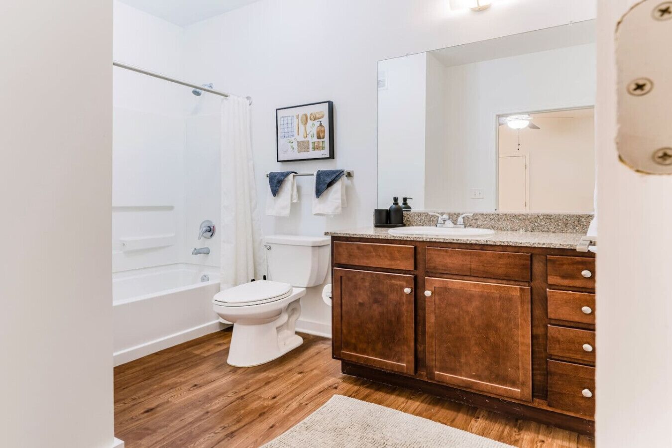 A bathroom with a white toilet, wooden cabinets, a large mirror, and a shower area.