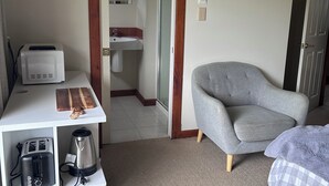 Een hotelkamer met kitchenette, een grijze fauteuil, een bed met ruitbeddengoed en een flatscreen tv aan de muur.
