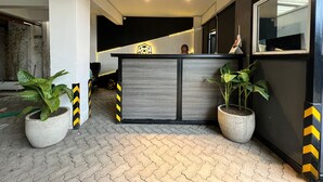 A reception desk with a modern design, flanked by potted plants, and a check-in counter with a digital display. - Triad Apartment (Nairobi)