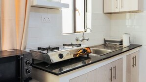 A compact kitchen with a gas stove, a microwave, and a sink. - Triad Apartment (Nairobi)