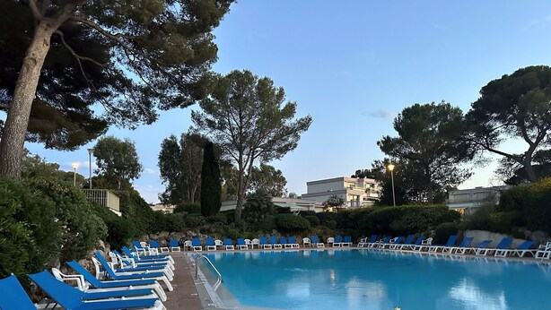 A pool area with blue and white lounge chairs arranged around a central pool, surrounded by trees and buildings in the background. - Duplex 6 pers 55m2 with swimming pool and sea nearby (Saint-Raphaël)
