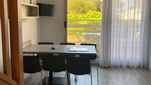 A modern kitchen with a dining area, a TV mounted on the wall, and a view of the outdoors through a large window. - Duplex 6 pers 55m2 with swimming pool and sea nearby (Saint-Raphaël)