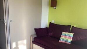 A room with a closed door, a green wall, a wooden floor, and a dark-colored sofa with two pillows. - Duplex 6 pers 55m2 with swimming pool and sea nearby (Saint-Raphaël)
