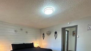 Une chambre à coucher comprenant un lit, une table de chevet, une horloge murale et une porte donnant sur une autre pièce.