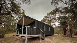 Una cabaña moderna y de color oscuro, con una terraza de madera y escaleras que conducen a un vestíbulo cubierto.