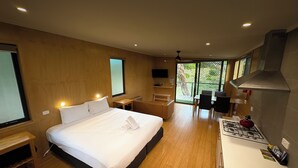 Una habitación de hotel moderna con una cama grande, un escritorio pequeño, una zona de comedor y una cocina con estufa a gas.