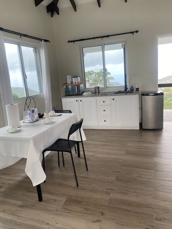 Una cocina moderna con armarios blancos, una mesa de comedor con sillas y grandes ventanales con vistas al exterior.