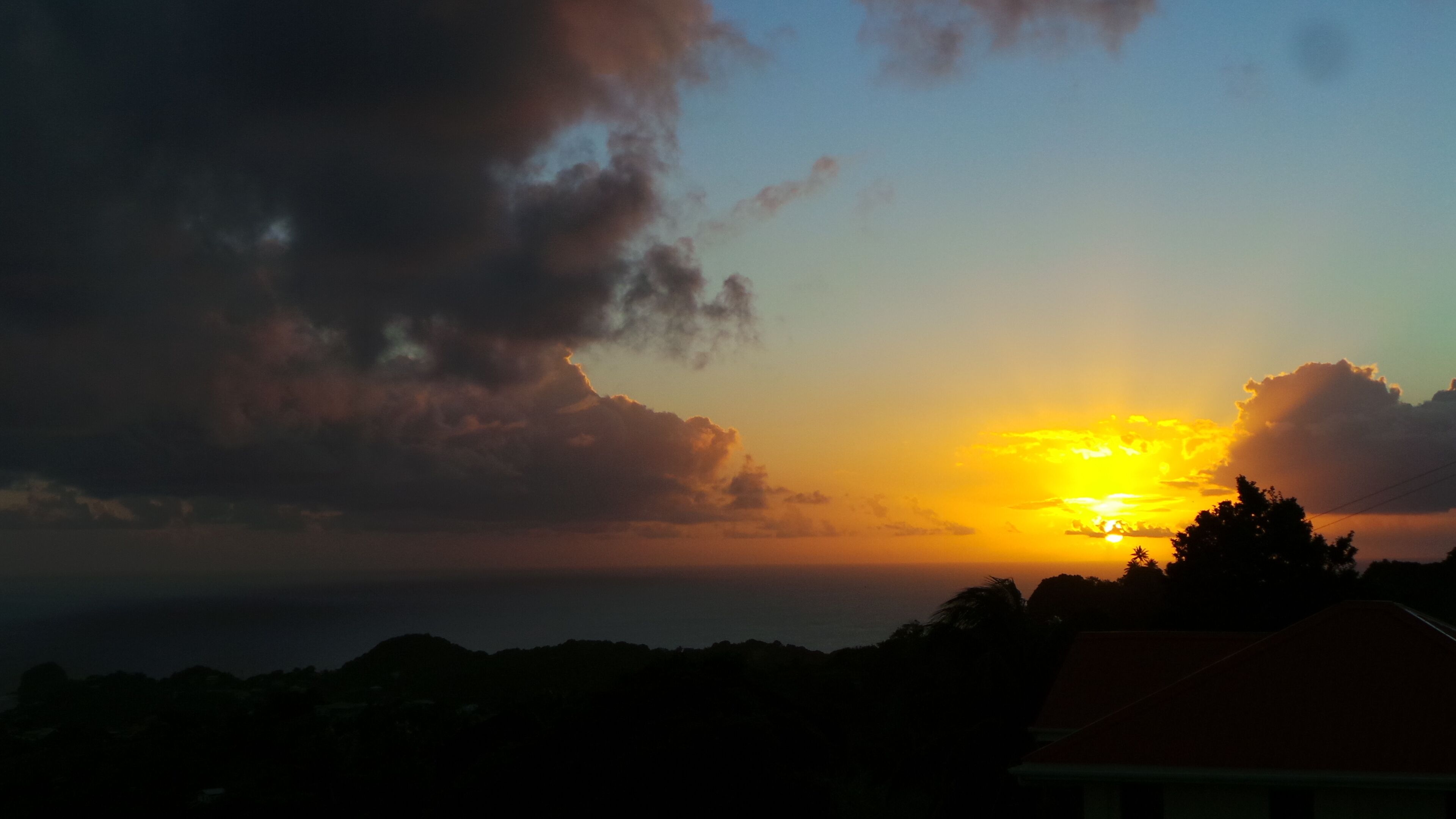 Um pôr do sol sobre uma paisagem com uma casa ao primeiro plano.