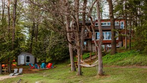 Una cabaña con un muelle, rodeada de árboles, y un cobertizo pequeño con asientos al aire libre.