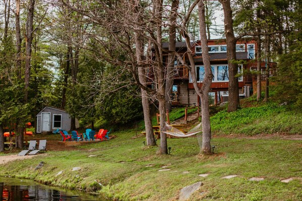 A cabin with a dock, surrounded by trees, and a small shed with outdoor seating.
