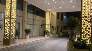 Een hotelentree met een modern ontwerp, met een glazen gevel, een goed verlichte inkomruimte en potplanten.