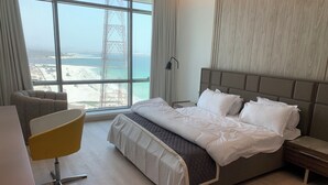 Een hotelkamer met een groot bed, een stoel, een bureau en uitzicht op het strand en een toren.