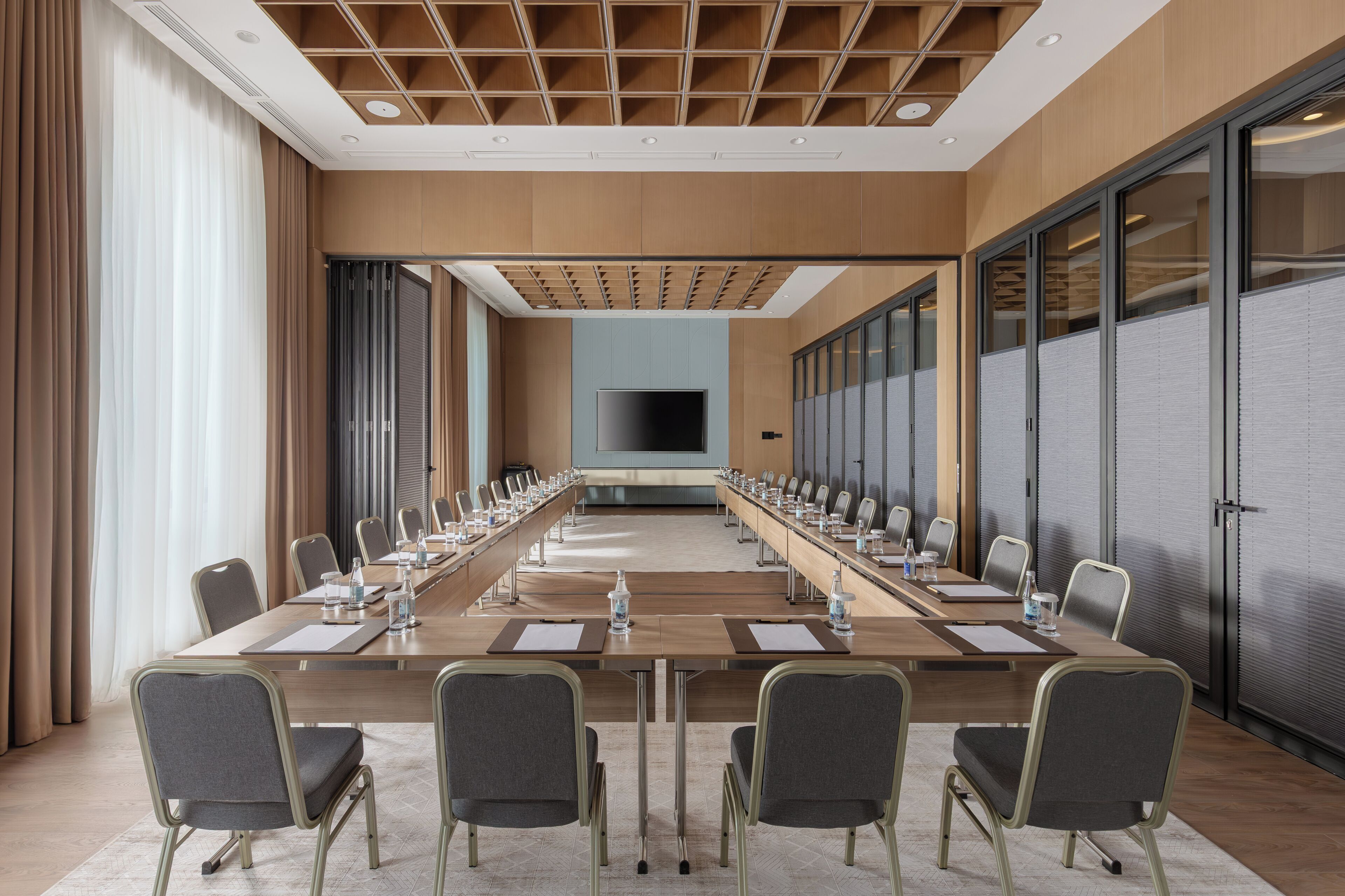 A conference room with a long table, chairs, a flat-screen TV, and a large window.