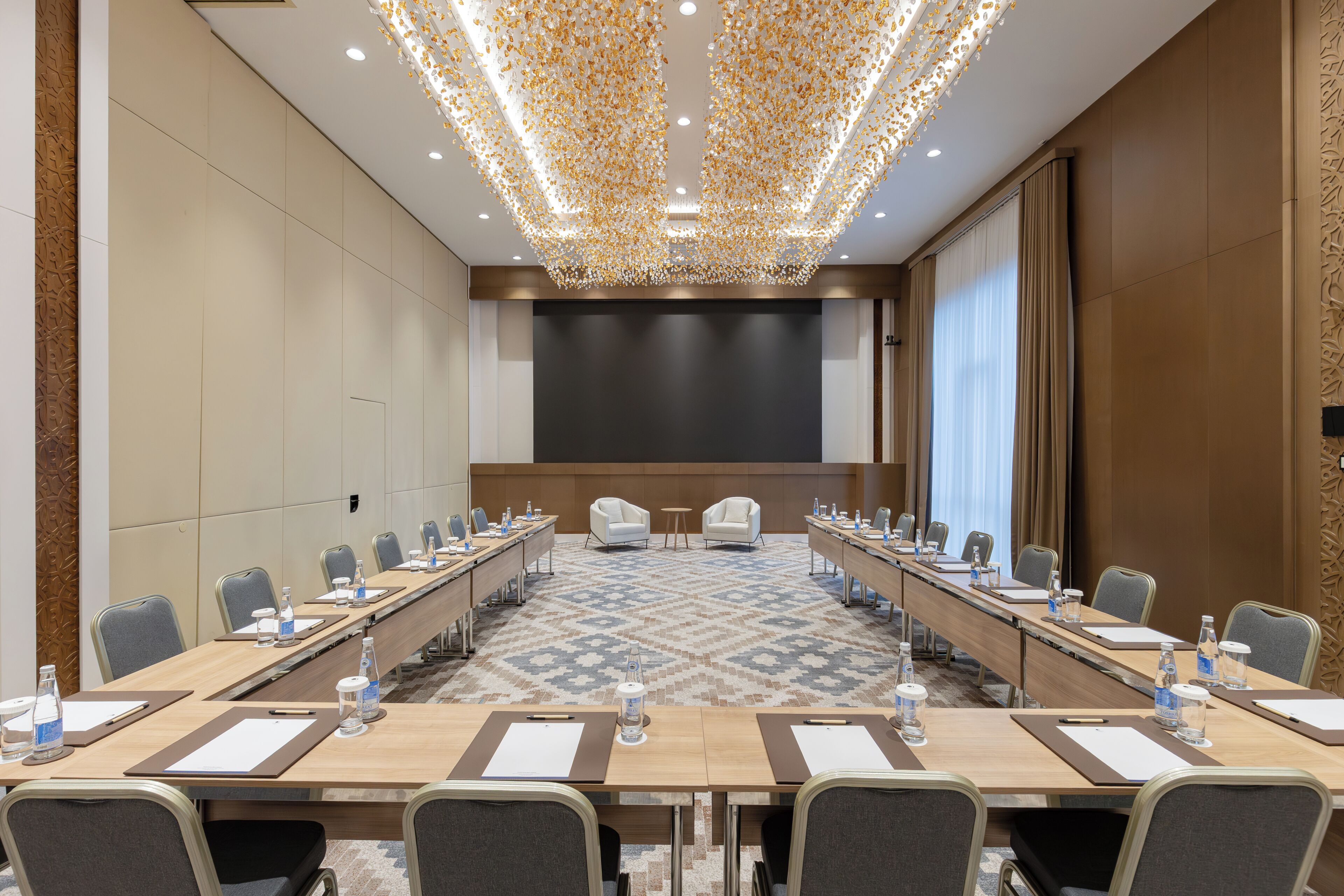 A conference room with a long table, chairs, a projector screen, and a patterned carpet.