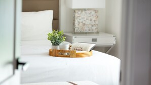 A neatly made bed with a white comforter, a bedside table with a lamp, and a small potted plant.
