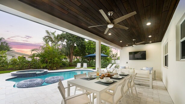 An outdoor patio with a pool, white furniture, and a ceiling fan.