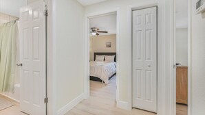 A hallway leading to a bedroom with a bed, a ceiling fan, and a door.
