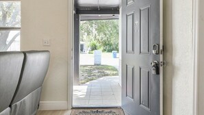 A room with a grey door, a window, and a view of a garden outside.