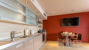Eine moderne Küche mit Essbereich, ausgestattet mit einem Flachbildfernseher an der Wand, einer Spüle aus Edelstahl und Holzschränken.