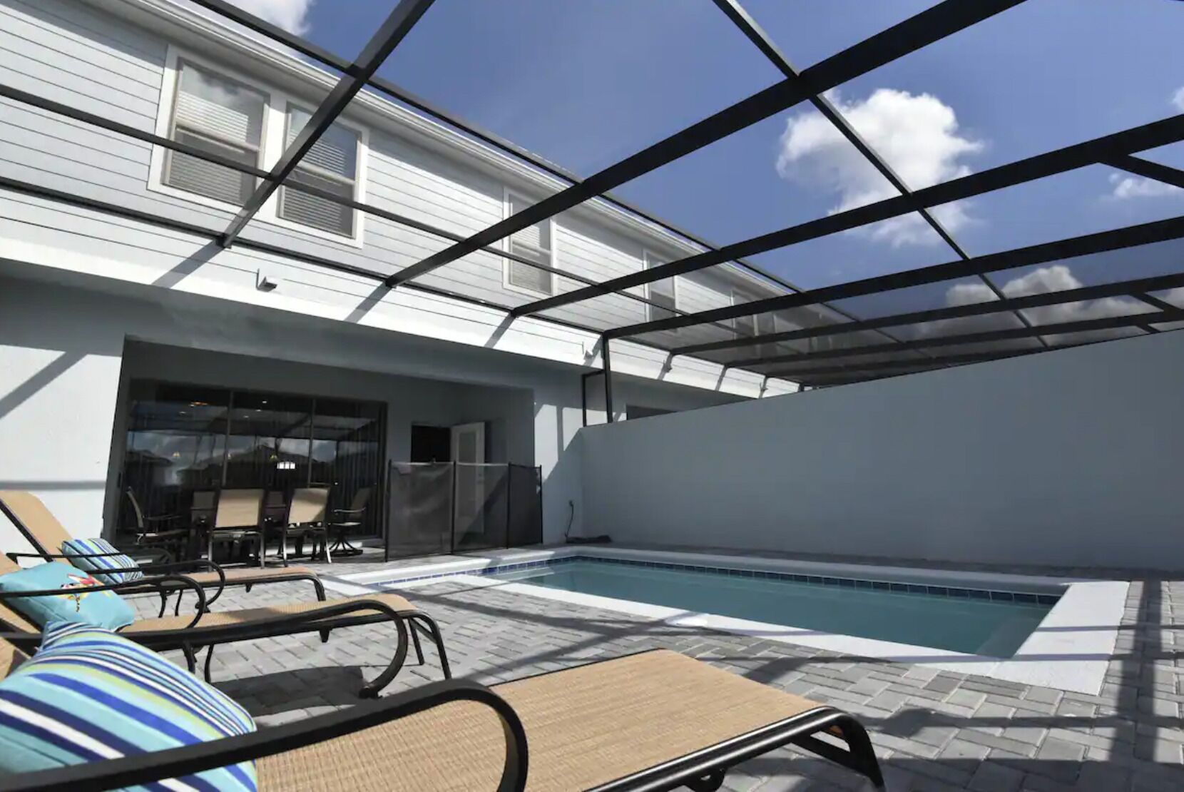 Een overdekt buitenzwembad met ligbedden en een patio met glazen wanden.