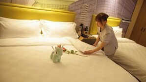 Una habitació d'hotel amb un capçal de llit groc, un llit amb roba de llit blanca i un joguet suau al llit.