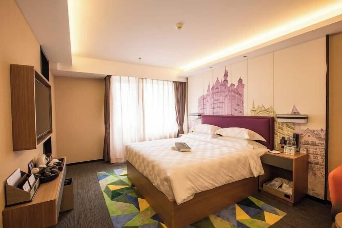 A hotel room with a bed, a desk, a TV, and a window with curtains.