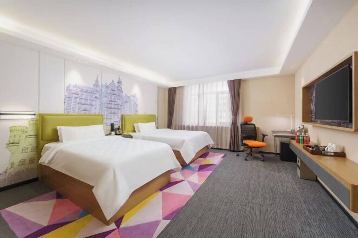 A hotel room with two beds, a desk, a chair, a TV, and a large window with curtains.