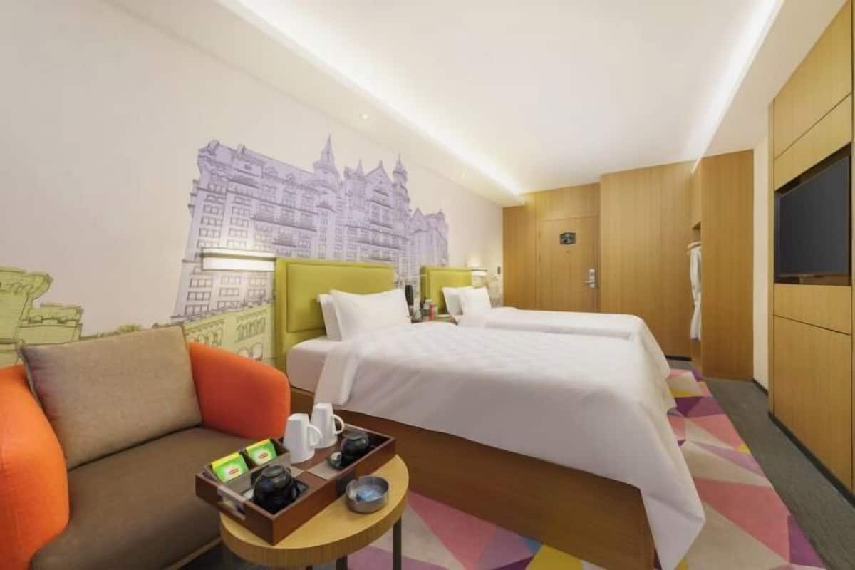 A hotel room with two beds, a sofa, a small table with items, and a mural of a cityscape.