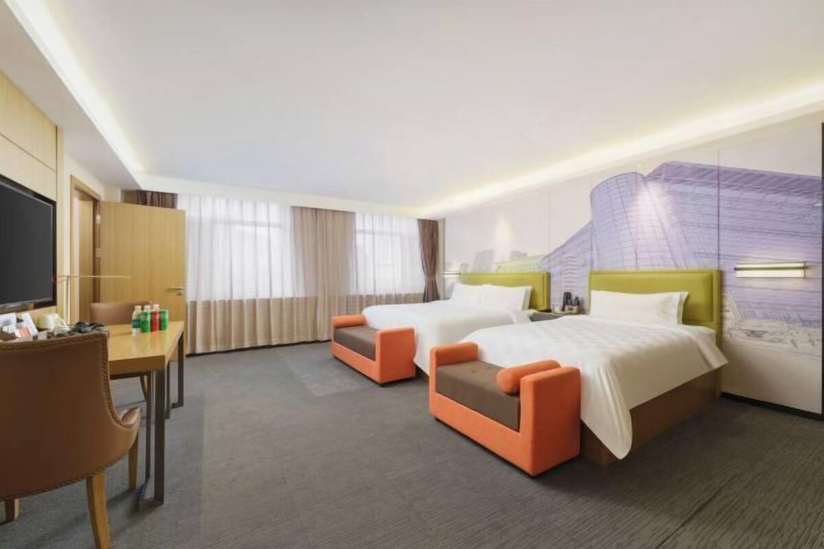 A hotel room with two beds, a desk, a chair, and a television.