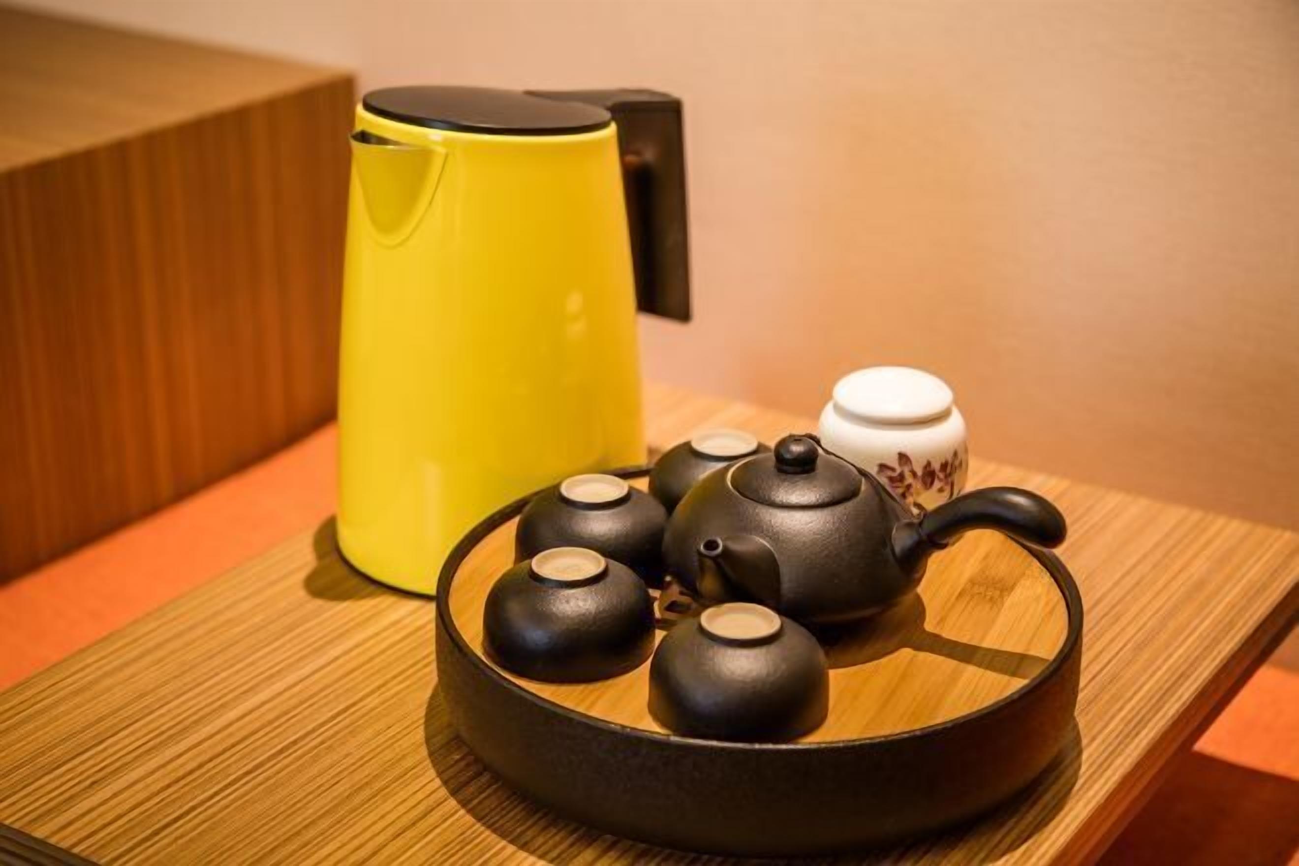 A set of black teapots and a yellow kettle on a wooden tray.
