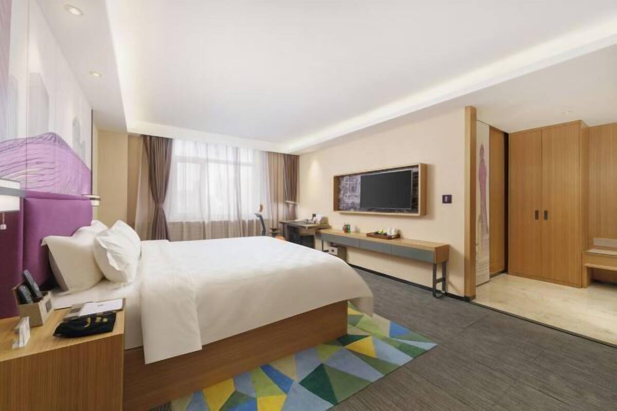 A hotel room with a bed, a desk, a TV, and a wardrobe.