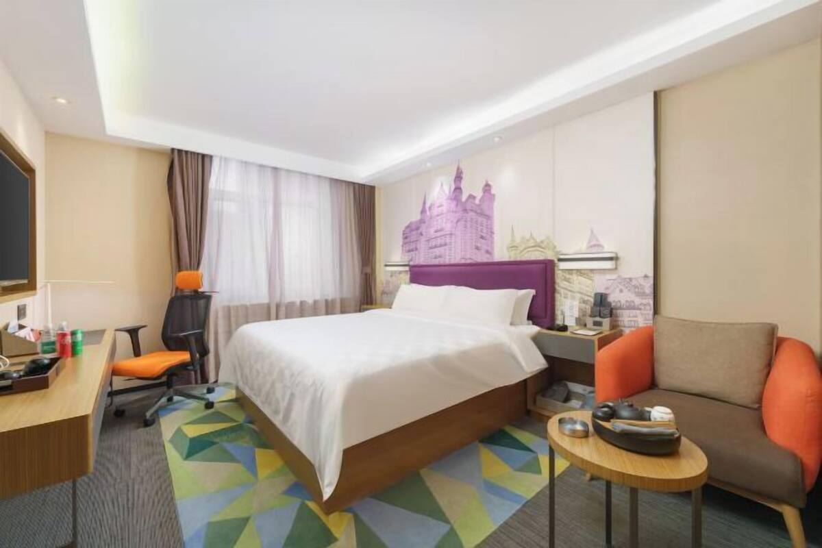 A hotel room with a bed, a desk, a chair, a small table, and a sofa.