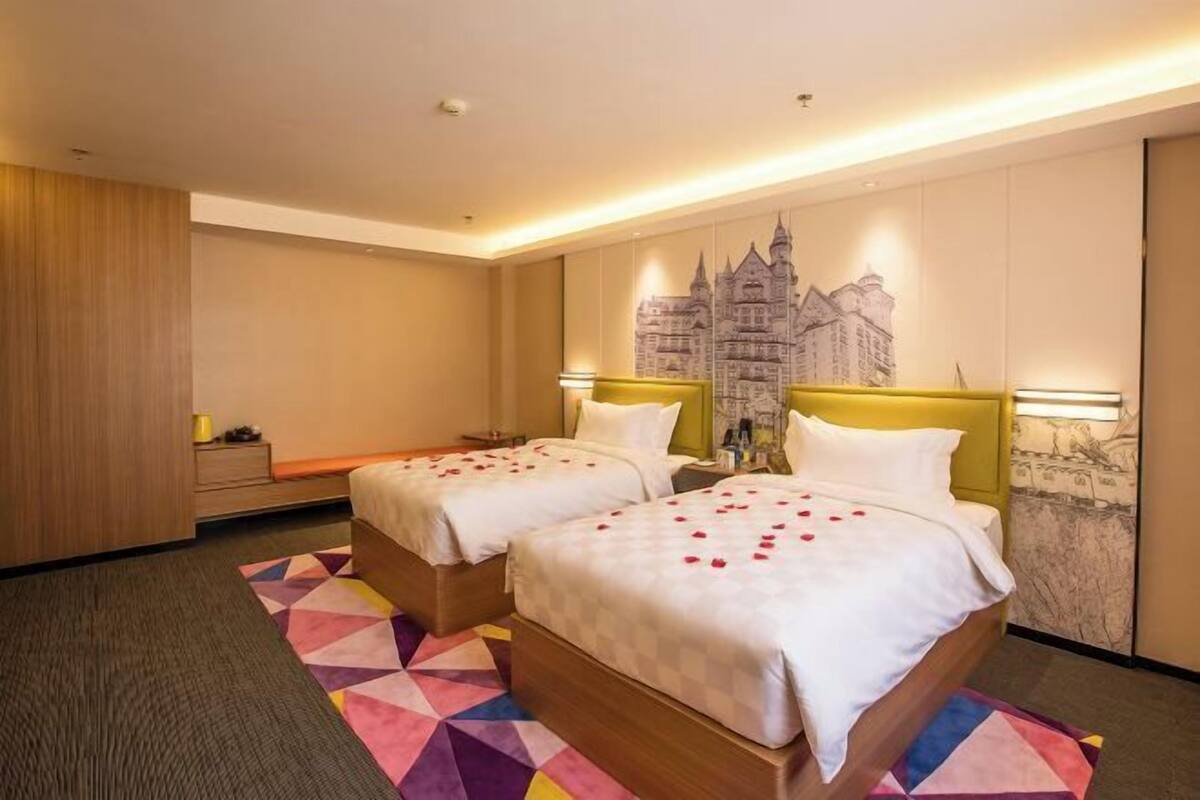 A hotel room with two beds, a wooden headboard, a colorful geometric rug, and a wall mural.