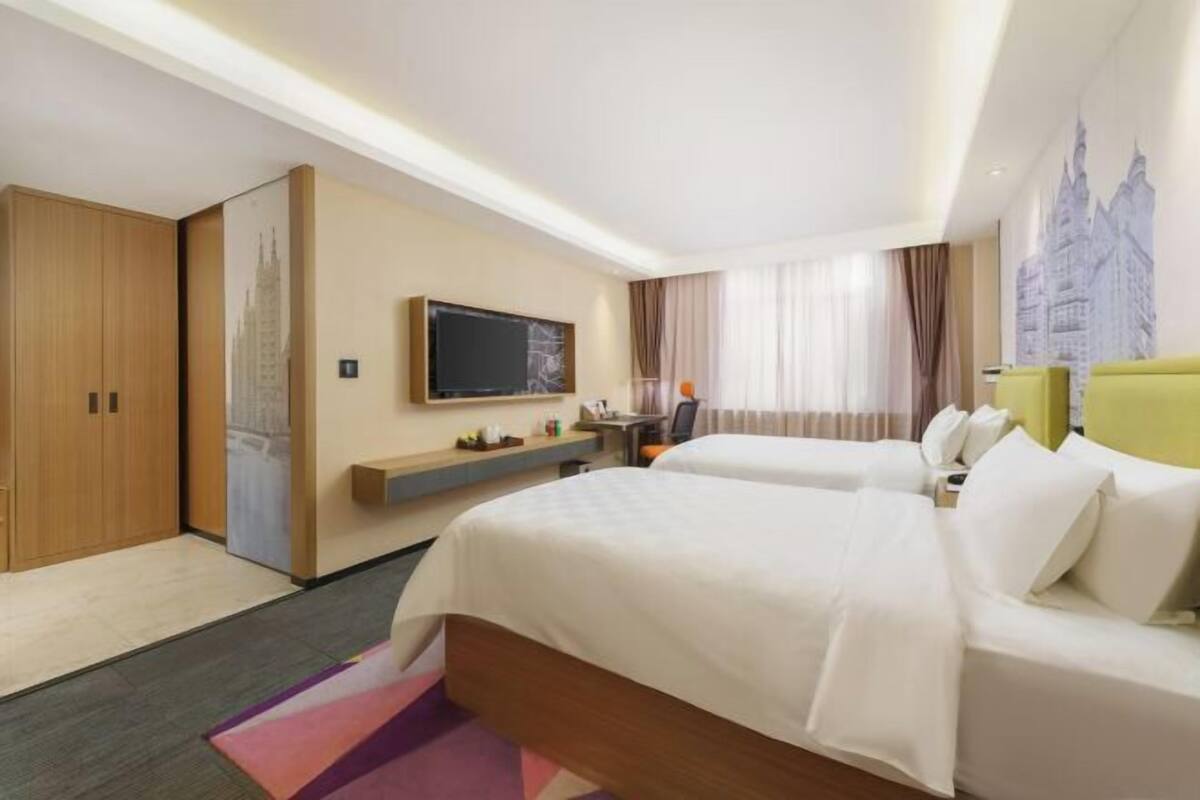 A hotel room with two beds, a desk, a TV, and a cityscape mural.