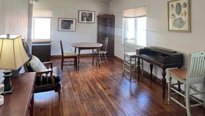 Una habitación amplia con pisos de madera, una mesa de comedor con sillas, un piano y obras de arte enmarcadas en las paredes.