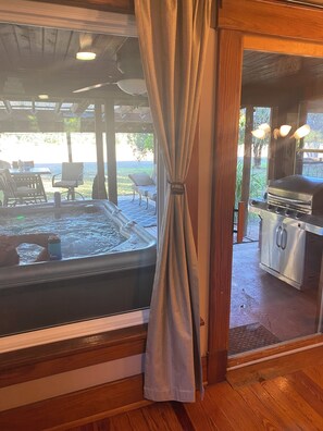 A hot tub with a view of a patio area, a grill, and a covered seating area.